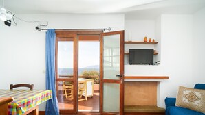 Una habitación con una mesa de comedor, un sofá, un televisor montado en la pared y un ventanal corredizo que da a un espacio exterior.
