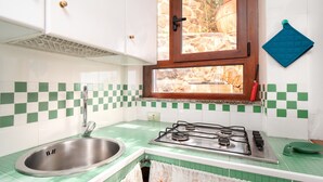 Una cocina con un lavaplatos de acero inoxidable, una estufa a gas y una ventana con vista a un muro de piedra.