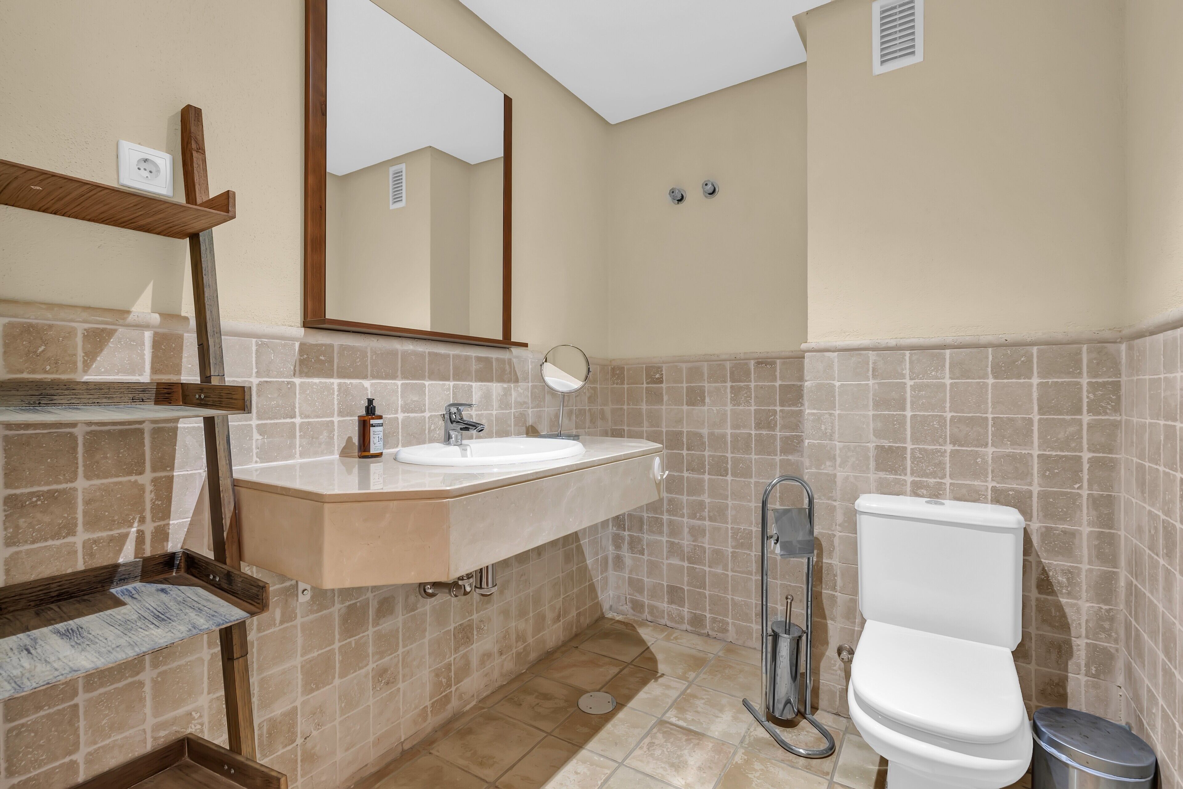 A bathroom with a sink, mirror, toilet, and tiled walls.