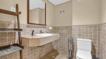 A bathroom with a sink, mirror, toilet, and tiled walls.