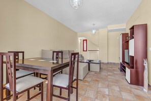 A dining area with a wooden table and chairs, a sofa, a TV stand, and a staircase leading to another level.