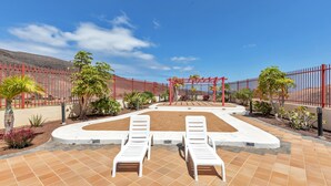 Ein Poolbereich mit zwei weißen Liegestühlen, einem roten Zaun und einer Pergola.