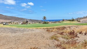 Ein Golfplatz mit blauem Himmel, weiter Meerlinie und trockener Vegetation.