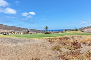 Golfkenttä, jonka yllä on kirkas taivas, horisontissa näkyy valtameri ja maasto on kuivaa kasvillisuutta.