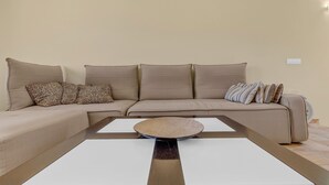 Ein beiges Sofa mit gemusterten und gestreiften Kissen, ein runder gewebter Couchtisch und ein weißer Beistelltisch.