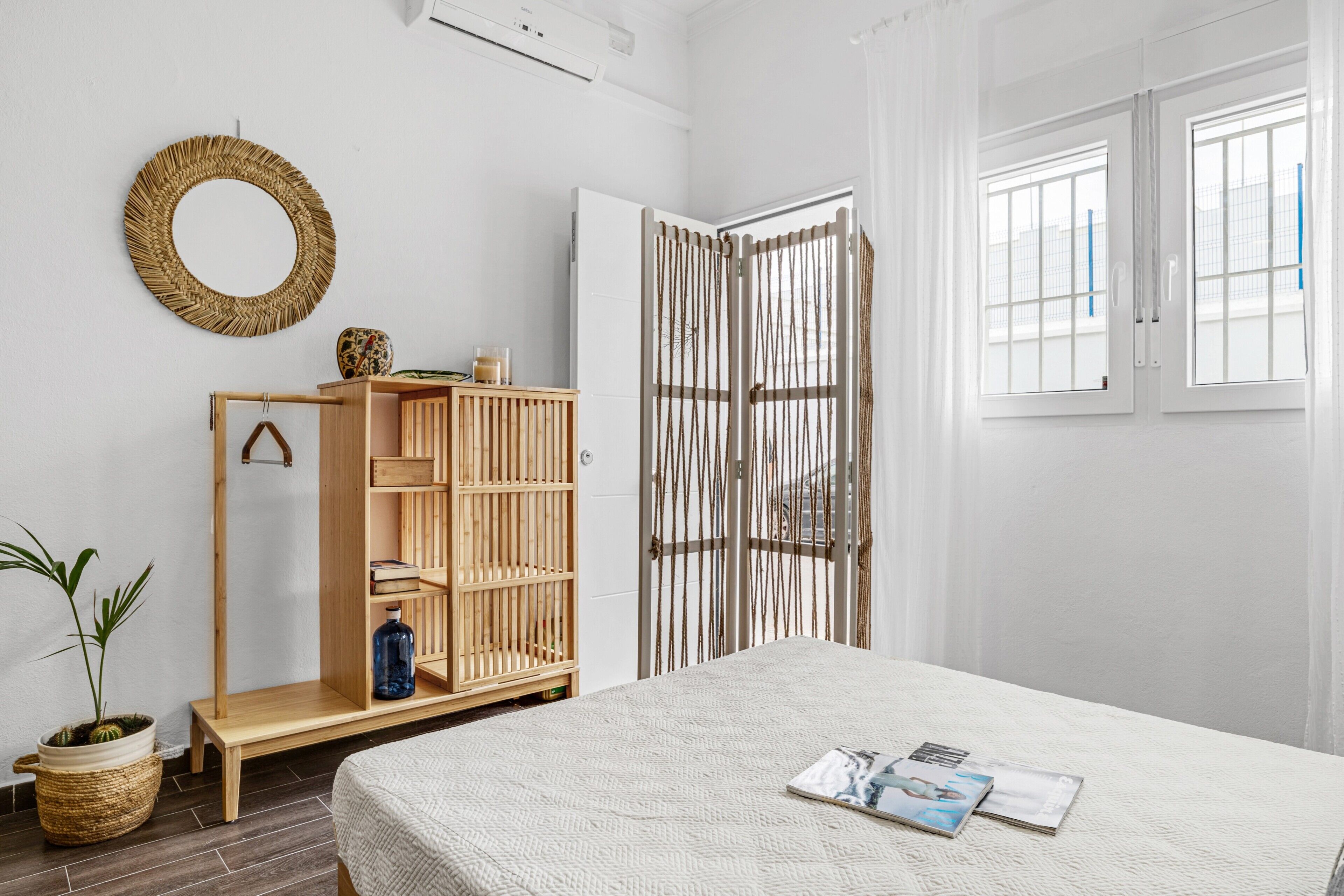 Ein Schlafzimmer mit einem Bett, einem Holzschrank, einem Weiden-Spiegel und einem Fenster mit Vorhängen.