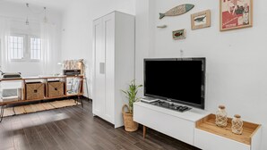 A modern living room with a flat-screen TV, a bookshelf, a white cabinet, and decorative wall art. - Studio Apartment 'La Casita Blanca' with Wi-Fi and Air Conditioning (Barbate)