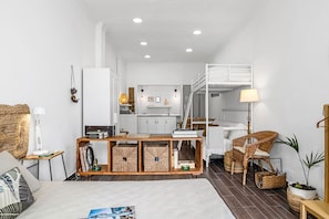 A compact living space with a bunk bed, kitchenette, and a cozy seating area with a wicker chair and a small table.