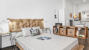 A modern bedroom with a large bed, a bedside table with a lamp, a wooden nightstand, and a built-in bookshelf. - Studio Apartment 'La Casita Blanca' with Wi-Fi and Air Conditioning (Barbate)