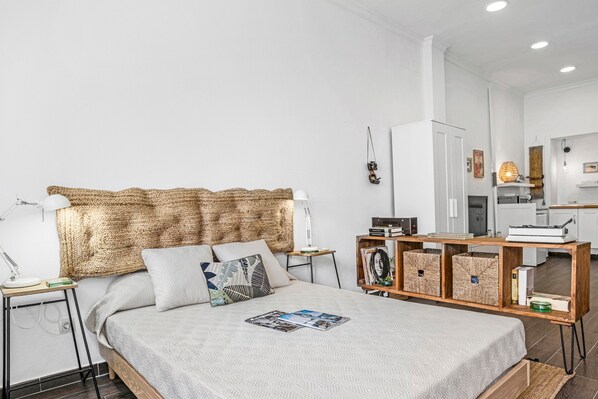 Une chambre moderne avec un grand lit, une table de chevet avec une lampe, une commode en bois et une bibliothèque intégrée.