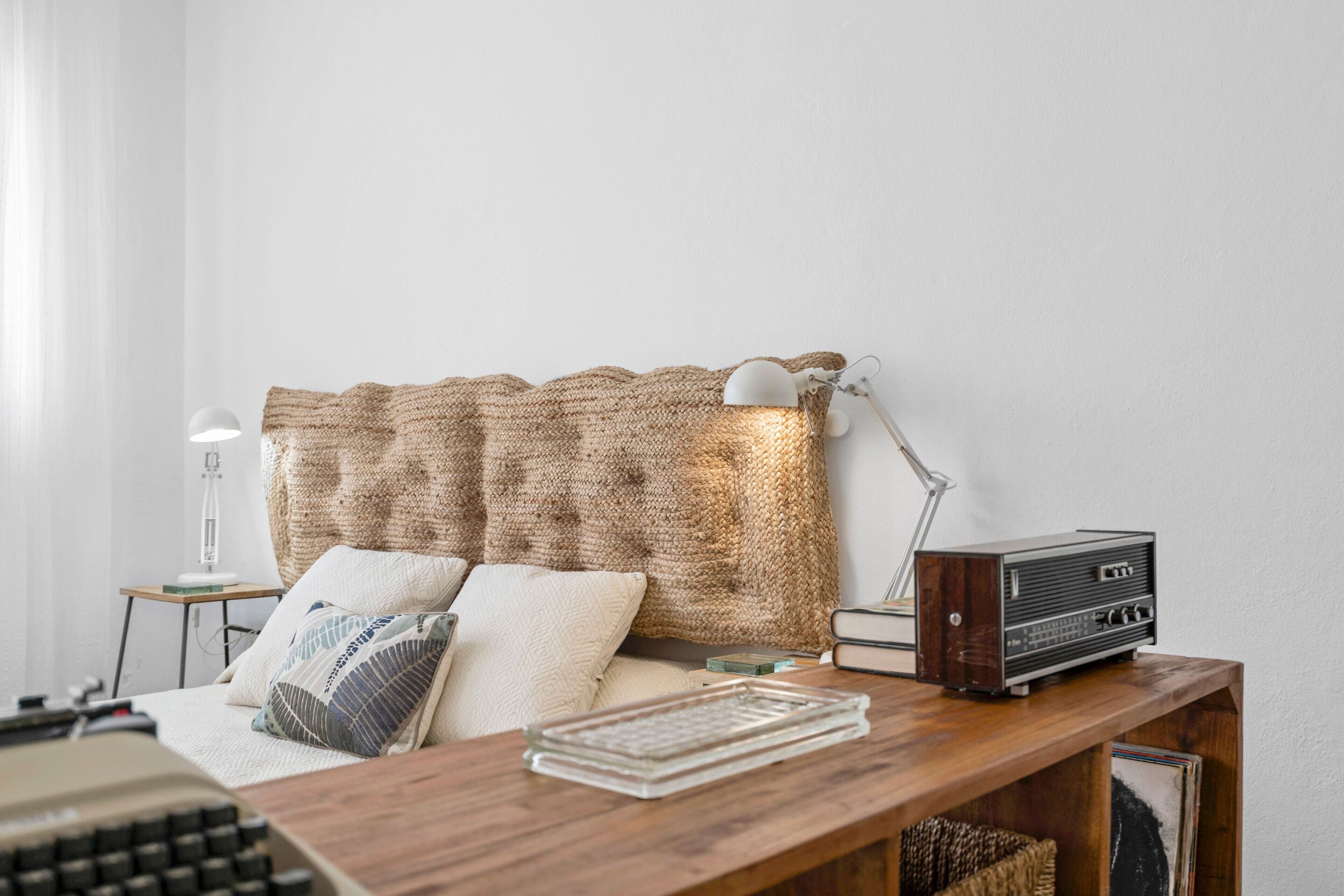 A room with a wooden desk, a vintage radio, a lamp, and a knitted wall hanging.