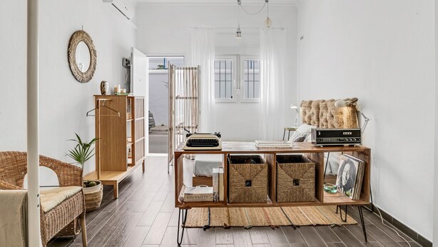 A modern living room with a wicker sofa, a wooden cabinet, and a small table with books and decorative items. - Studio Apartment 'La Casita Blanca' with Wi-Fi and Air Conditioning (Barbate)