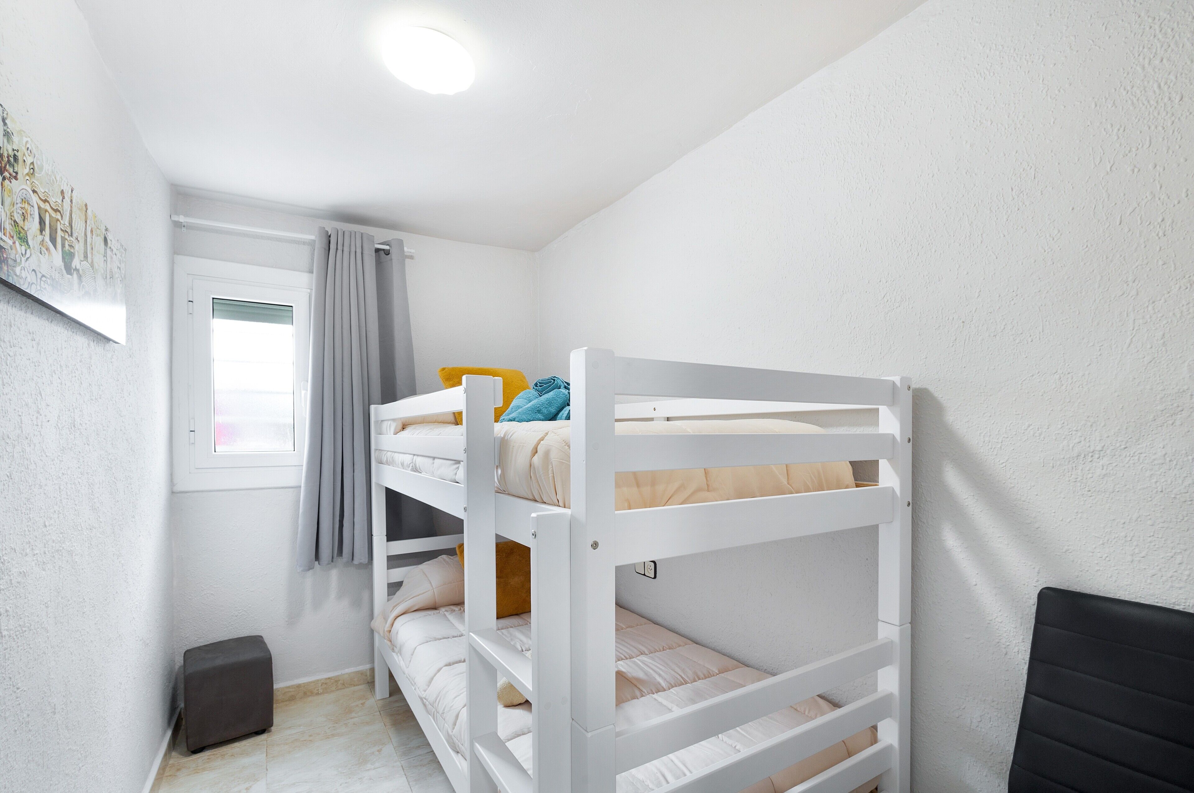 Een slaapkamer met een stapelbed, raam, gordijnen en een klein pouf.