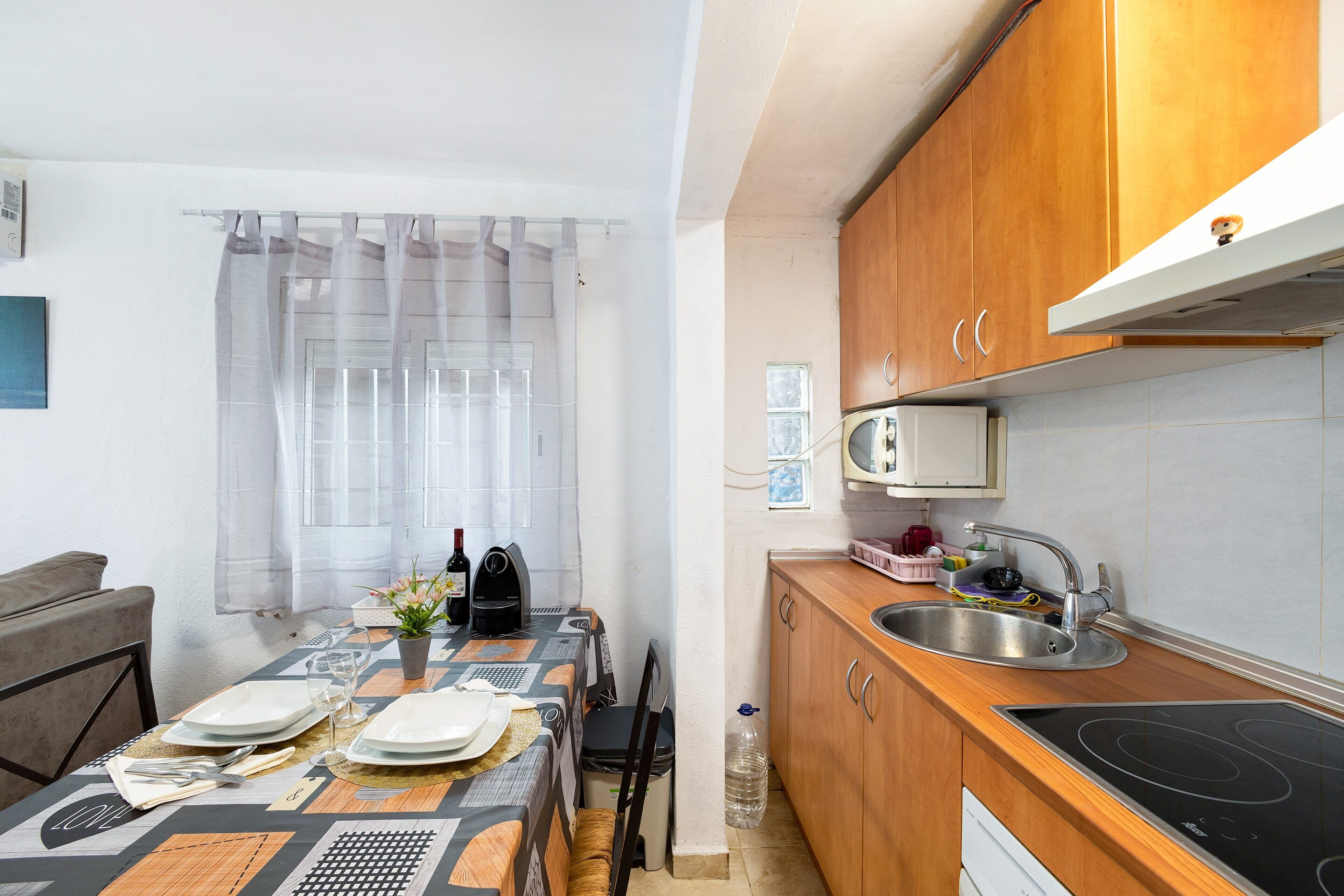 Cocina compacta con comedor, microondas, lavamanos y muebles de madera.