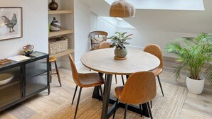 A dining area with a round table, chairs, a hanging light fixture, and a potted plant. - The Hermit Inn Hideout (Burley Woodhead, near Ilkley)