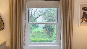A window with beige curtains, a stone arch above, and a view of a green landscape. - The Hermit Inn Hideout (Burley Woodhead, near Ilkley)