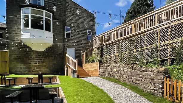 A stone building with a corner window, outdoor seating, and a wooden fence. - The Hermit Inn Hideout (Burley Woodhead, near Ilkley)