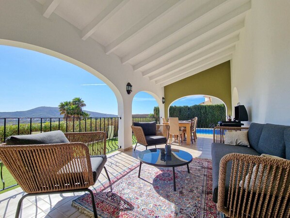 A covered outdoor seating area with wicker furniture, a pool, and a view of the landscape.