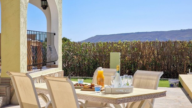 Un espace de restauration en plein air avec une table dressée pour deux personnes, une bouteille de jus d’orange et un plateau avec des verres et une bouteille de vin Zonin.