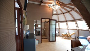 A modern, compact living space with a curved ceiling, a dining area, and a seating area with a rocking chair. - Countryside Getaway Sand UniqueDomeB/serene farm retreat (Snow Camp)