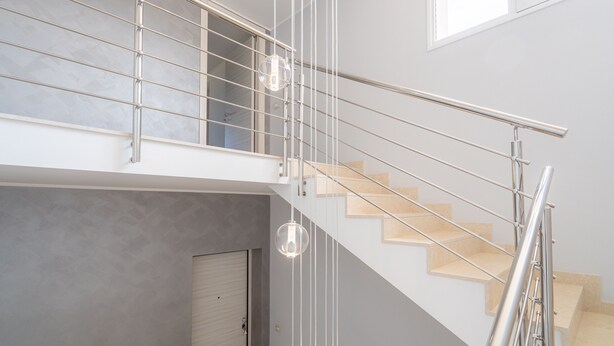 Una escalera moderna con barandilla de cristal y una lámpara colgante.