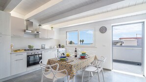 Una cocina moderna con armarios blancos, una mesa de comedor preparada para cuatro personas y un ventanal con vista al mar.