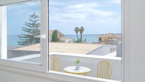 Un balcón con vista al mar, una planta en maceta y sillas amarillas.