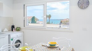 Una cocina con lavadora, una mesa de comedor con platos coloridos y una ventana con vistas al mar.