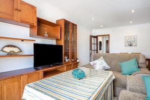 A living room with a television, wooden cabinets, a sofa, and a striped tablecloth.