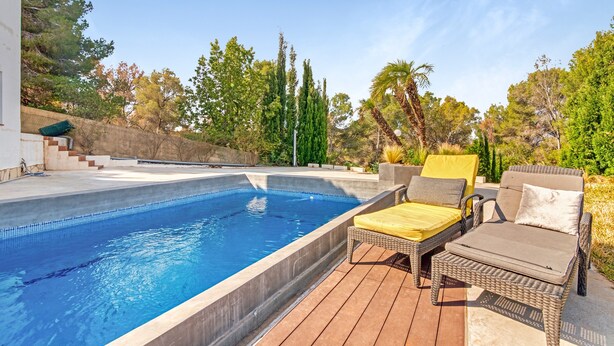 A swimming pool with a wooden deck, wicker lounge chairs, and a view of trees and a building. - Villa "Bohemia" with Sea Views, Private Pool, and Wi-Fi (Jávea)
