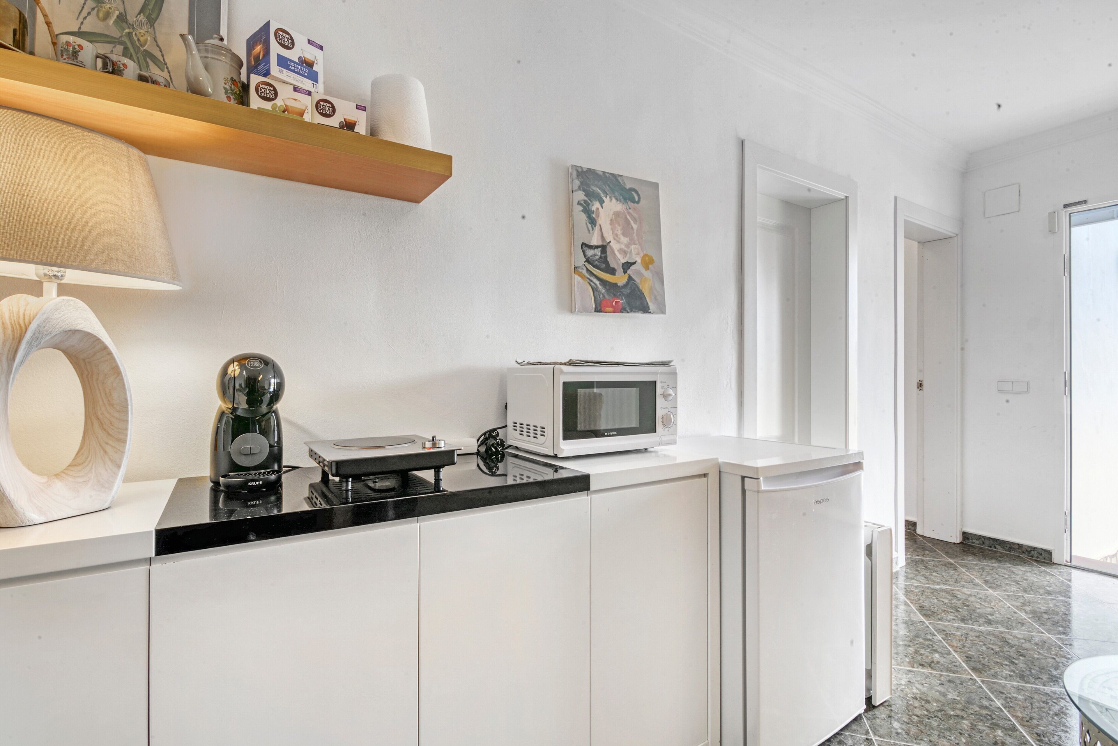 A kitchen with a microwave, coffee maker, and a painting on the wall.