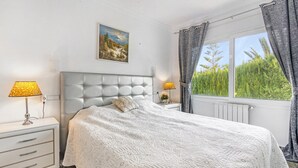 A bedroom with a tufted headboard, a bed with a white quilt, a nightstand with lamps, and a window with curtains. - Villa "Bohemia" with Sea Views, Private Pool, and Wi-Fi (Jávea)