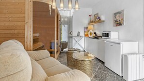 A modern interior with a wooden wall, a sofa, a kitchen area with a microwave, and a small table. - Villa "Bohemia" with Sea Views, Private Pool, and Wi-Fi (Jávea)
