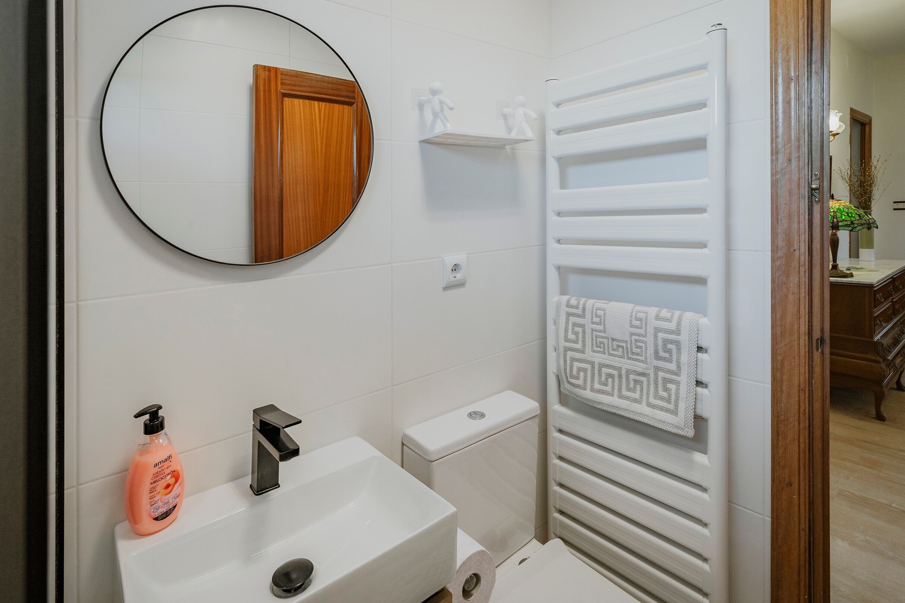 Een badkamer met een ronde spiegel, een wastafel, een toilet en een handdoekhouder.