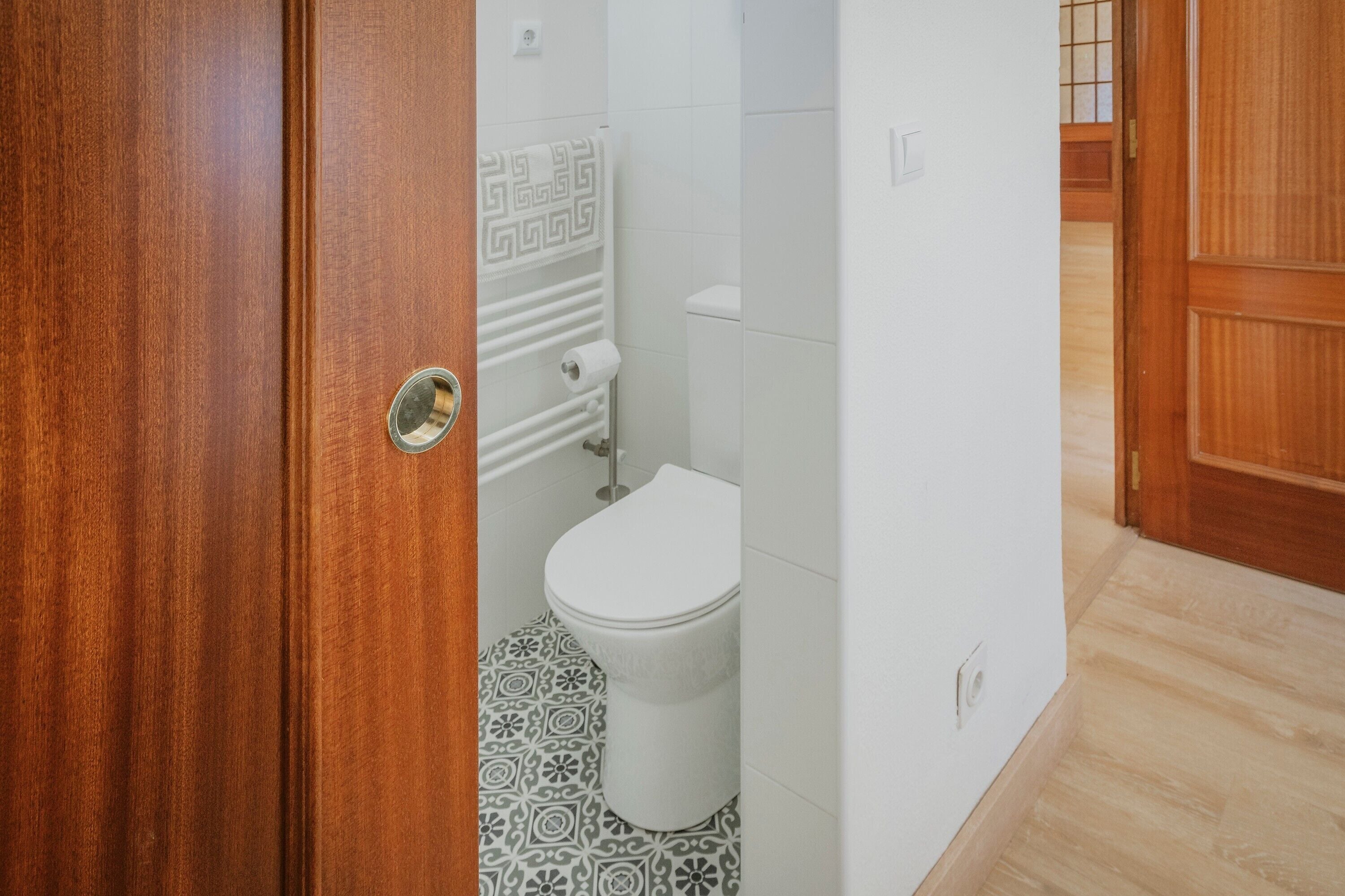 Une salle de bain avec des toilettes, des carreaux de sol à motifs, un porte-serviettes et une porte en bois.