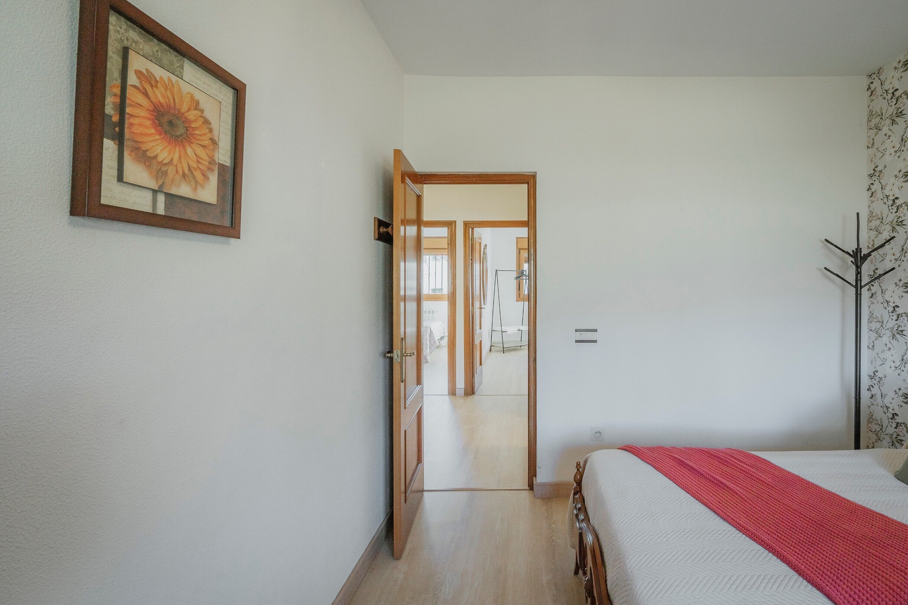 Een slaapkamer met een bed, een deur naar een gang en een ingelijst schilderij aan de muur.