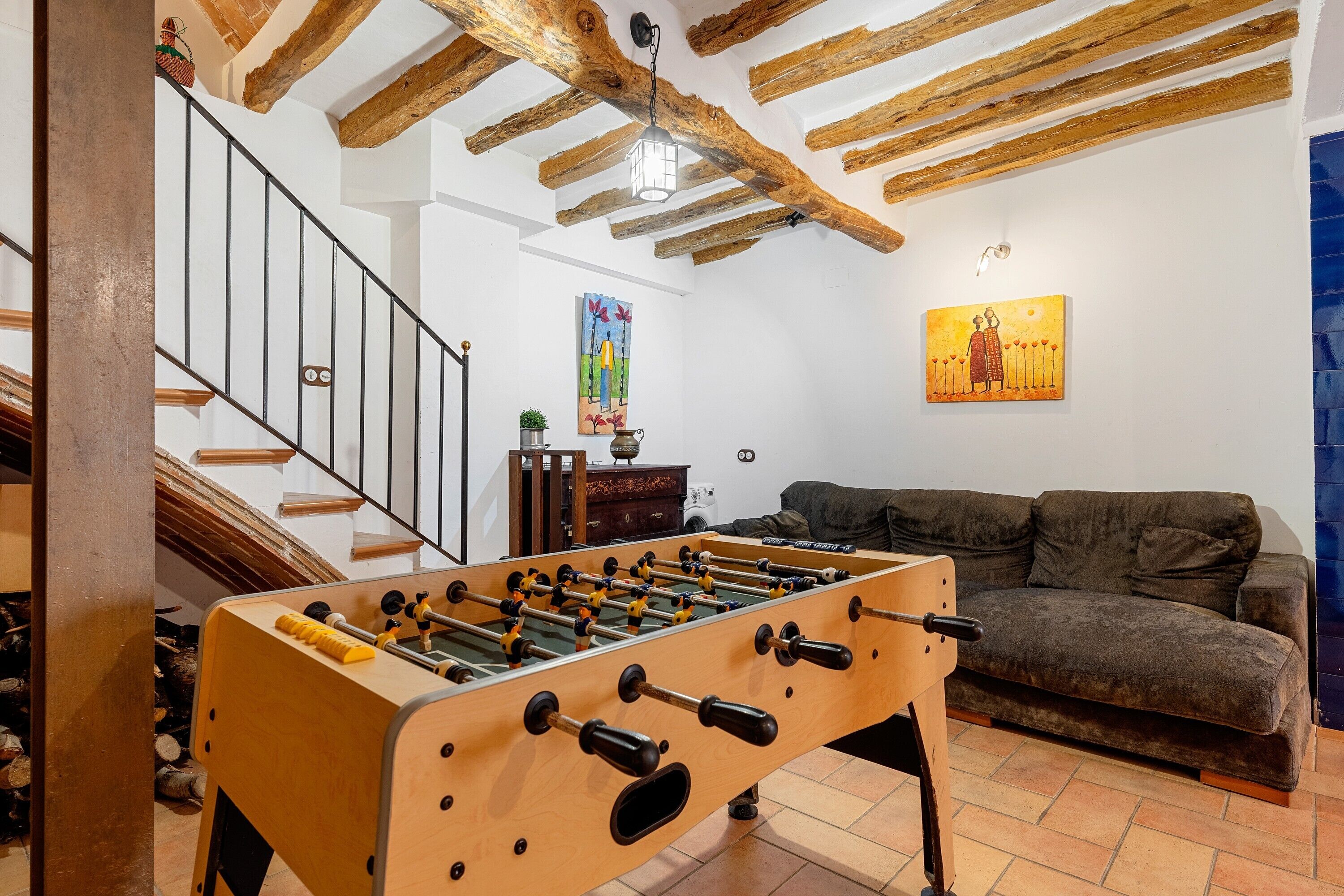 Una habitación con mesa de fútbol, sofá, escalera y un cuadro en la pared.