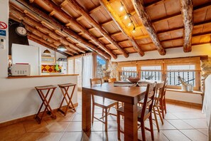Una cucina rustica con travi in legno, un tavolo da pranzo, sedie e una vista dalla finestra.