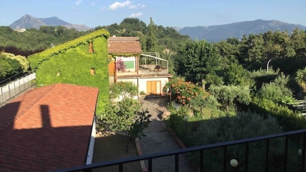 Una casa dal tetto rosso, circondata da vegetazione lussureggiante e con una montagna sullo sfondo.