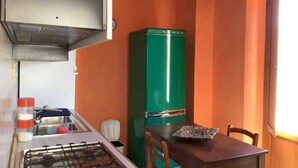 Una cucina compatta con piano cottura a gas, lavandino, frigorifero verde e tavolo con sedie.