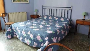Una camera da letto con un letto, un termosifone, due comodini, una sedia e un quadro appeso al muro.