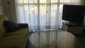 Un soggiorno con divano, tavolino in vetro, televisione e una finestra con tende leggere.