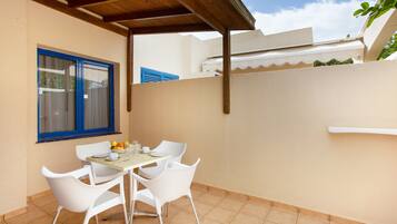 Un patio con una mesa y sillas, una ventana con contraventanas azules y un toldo blanco.