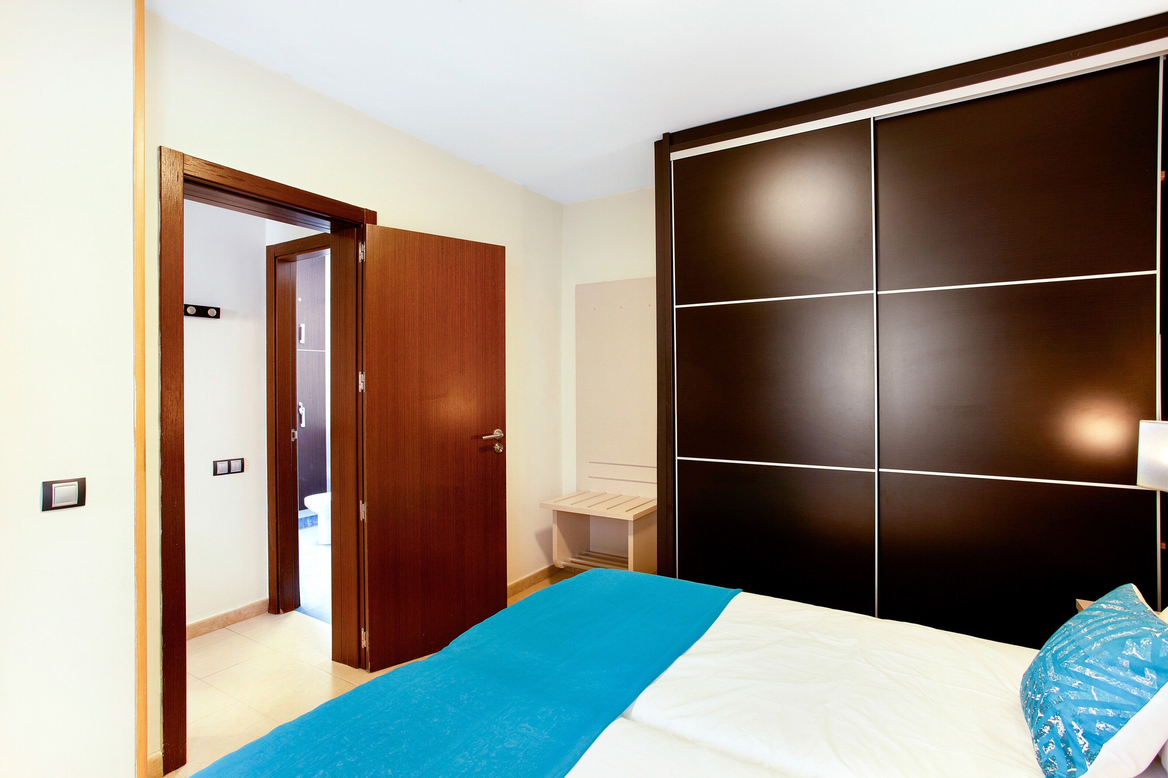 A bedroom with a bed, a wardrobe, a door, and a small bedside table.