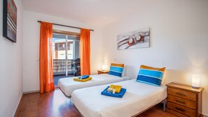 Habitación de hotel con dos camas, un balcón, un cuadro y una mesita de noche con lámpara.
