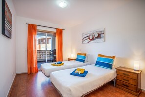 Camera d'albergo con due letti, un balcone, un quadro e un comodino con una lampada.