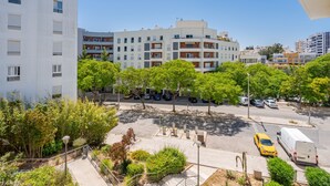Un edificio de varios pisos con balcones, un estacionamiento con automóviles y un paseo peatonal con árboles.