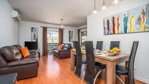 Una sala de estar moderna con un sofá de cuero marrón, una mesa de comedor con sillas, un televisor de pantalla plana y obras de arte en las paredes.