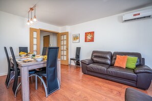 Un coin repas avec une table et des chaises en bois, un canapé en cuir et un appareil de climatisation fixé au mur.