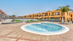 A pool area with a circular pool, a palm tree, and a row of yellow buildings with balconies.